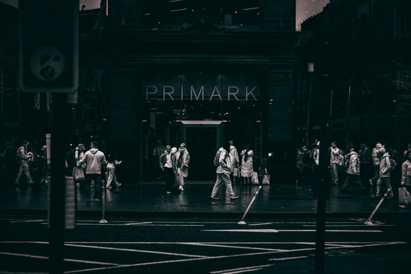 This image captures a desolate city street, stripped of warmth and color through deep infrared. Pedestrians, ghostlike and pale, move mechanically across a crosswalk, their winter coats stark against the dark, looming façade of a massive building. Its windows are lifeless and empty, a hollow monument to a system that no longer functions. The road markings remain crisp, and bent traffic poles lean inward, hinting at decay. Yet the crowd continues to obey invisible rules—stopping, walking, and spacing themselves with mechanical precision. No signals flash, no lights command them, but their movements persist as if dictated by an unseen authority. The figures are small and faceless, their steps hollow and automatic, caught in a rhythm they can’t escape. The scene feels frozen in time, heavy with silence, where obedience lingers not through power, but through patterns so deeply etched they endure long after the system fades away.