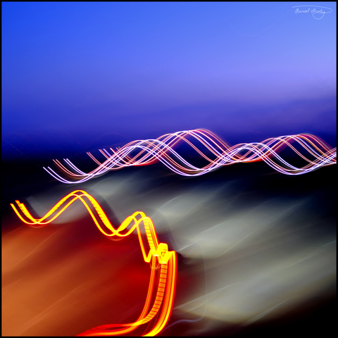 Long exposure of a motorway at dusk with intentional camera movement (ICM). The lights of the cars form different waves. A dark blue night sky can be seen at the top.