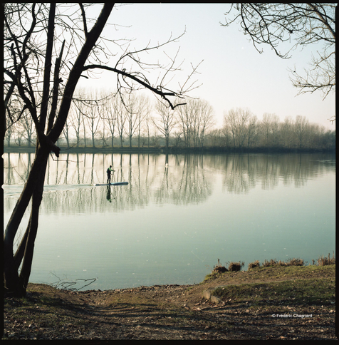 A wide view of the Saône River in late autumn, the waters are still, someone goes up the river on his stand-up paddle board. Photo taken with a 6x6 medium format camera on color negative film.