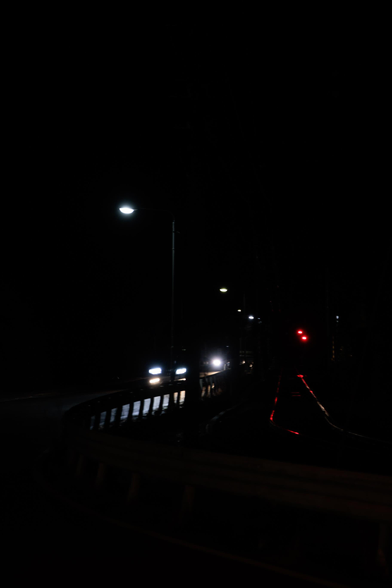 A dark street at night with streetlights and car headlights visible, and a red traffic signal.