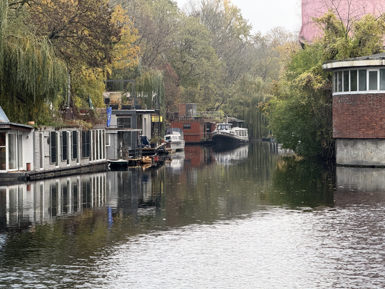 A brook, with houseboats docked on the left side, many of the houseboats have willows growing over them.

Photo taken in Charlottenburg.