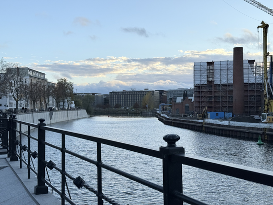 The river Spree as seen from a quay wall on the left. Further on the left you see apartment buildings on top of a quay wall. On the right you see early 20th century industrial buildings. In the middle you see an office building in the distance. The river itself is reflecting the blue sky.

Picture taken in Moabit.