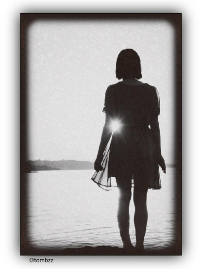 A girl stands on the shore of a bay, facing away from the camera. The sun's rays create a bright flare through her dress. The scene has a vintage, grainy effect, and the background shows a calm body of water with a distant shoreline. The image is framed with a dark border.