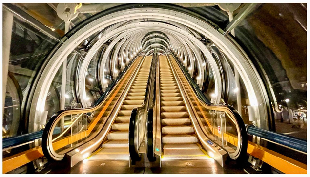 An illuminated escalator at the Centre Pompidou in Paris ascends within a futuristic, circular glass enclosure. The structure features metallic curves and lighting, creating a modern aesthetic. 