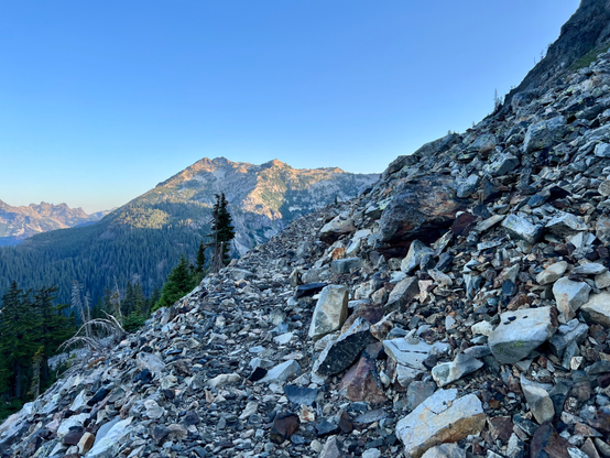 Rocky trail along the Alpine Lakes section of the PCT. Rocky mounts and blue sky behind the trail.