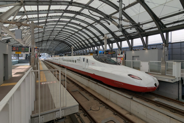 Am gegenüberliegenden Bahnsteig wartet ein Hochgeschwindigkeitszug mit langer Nase.
Oben hat er eine weisse Farbe. Unten ist er  rot. 