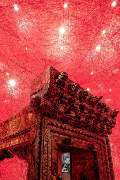 red string crisscrosses to wrap an elaborately carved structure