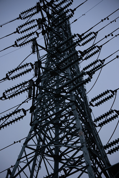 Close-up of a towering powerline structure against a darkening sky, featuring numerous insulators and cables.