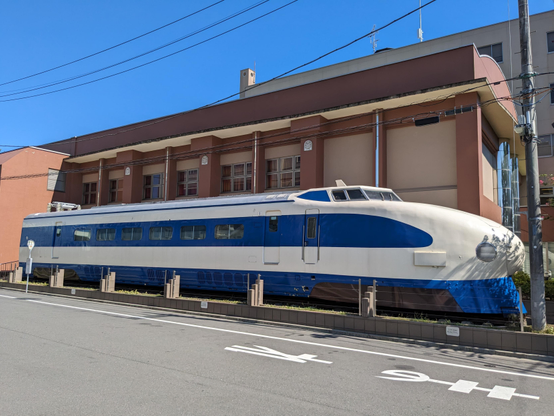 Ansicht des Shinkansen Triebkopfs von der Seite, mit dem Gebäude des Museums im Hintergrund.