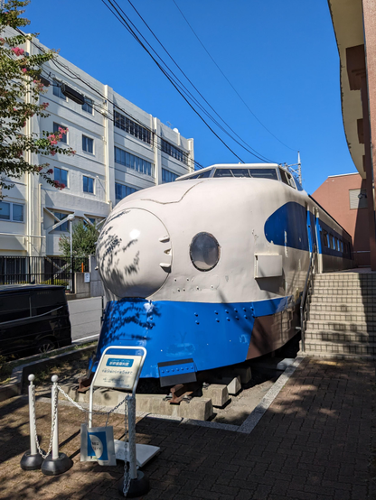 Shinkansen leicht seitlich von vorne mit einem Schild welches auf Museum und Öffnungszeiten Hinweise gibt.  