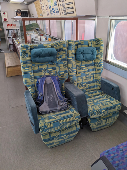 Eine Sitzgruppe in diesem ausgestellten Zug. Bequeme Polstersessel in gelb/blau gehalten.
Auf dem linken Sitz liegt mein Rucksack.
Dahinter ist ein Teil der Ausstellung im Zug zu sehen. 