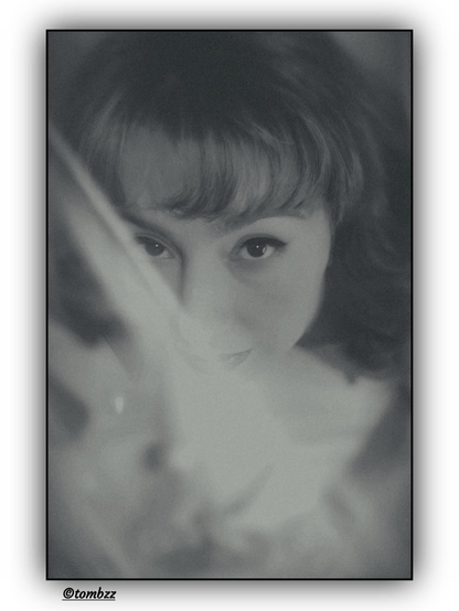 A monochromatic vintage-style portrait of a young woman. Her intense gaze draws attention, while the slightly high-angle shot adds depth and drama. Part of her face, including her lips, is gently veiled by a translucent fabric, giving the image an air of mystery. Her hair is medium-length, wavy, styled into loose curls that gracefully fall over her shoulders, enhancing the retro aesthetic of the photograph.