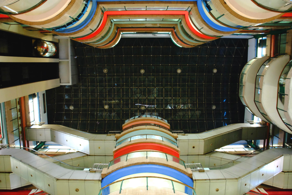 A window up a large hall with floors to all four sides. There are several balcony like structures in various colours as well as staircases and an elevator. where one would expect sky, there is a glass roof, it seems to be dark outside 