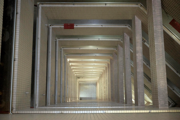 A photo down many levels of a high building. It goes down far, surrounded by balconies tiled with white plates. There is light on the lower levels, the image is mostly white 
