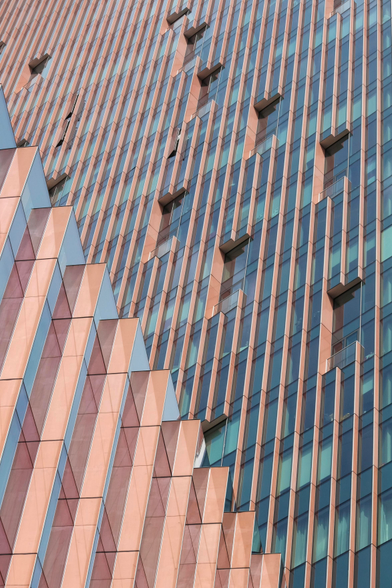 A photo of several walls, maybe representing a skyscraper with red-brown sides and long vertical window stripes. Two different walls are visible, both run in very different angles to another 