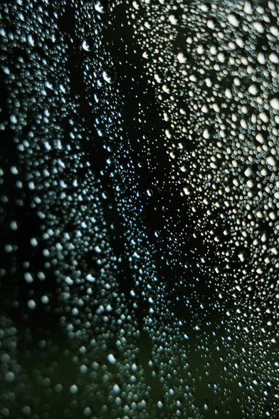 Close-up of water droplets on a dark surface, creating a textured, reflective pattern with varying light reflections.