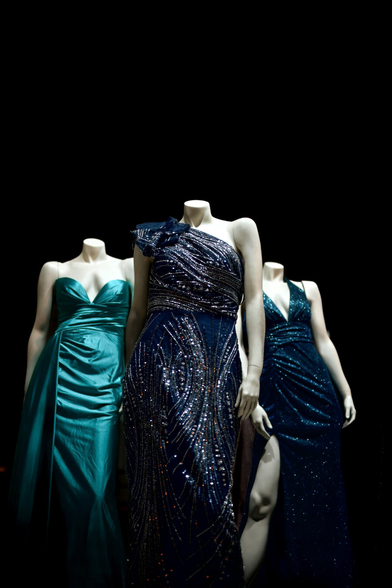 Three headless femme mannequins in shining dresses appear to strut out of the darkness toward camera
