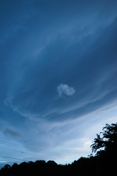 A dramatic twilight sky features swirling blue clouds with a soft, white cloud in the center, framed by dark tree silhouettes below.