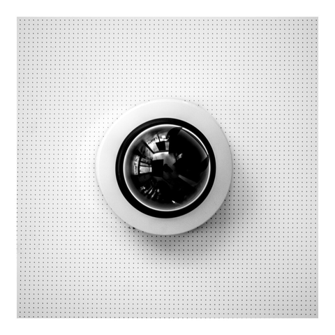 a shot of a black, round surveillance camera on the white perforated ceiling of a bank. It reminds of HAL from 2001 A Space Odyssey
