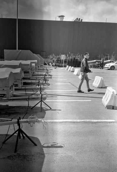 In a monochrome photo, a man walks past car trailers.