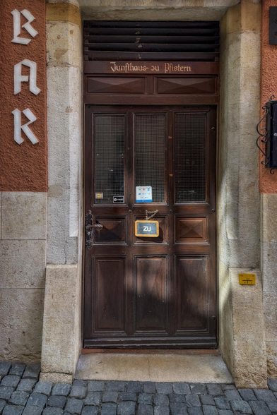 Hochformatfotografie einer Tür mit einem Wendeschild "ZU"; oberhalb die Beschriftung "Zunfthaus zu Pfistern", links vertikal "BAR". 