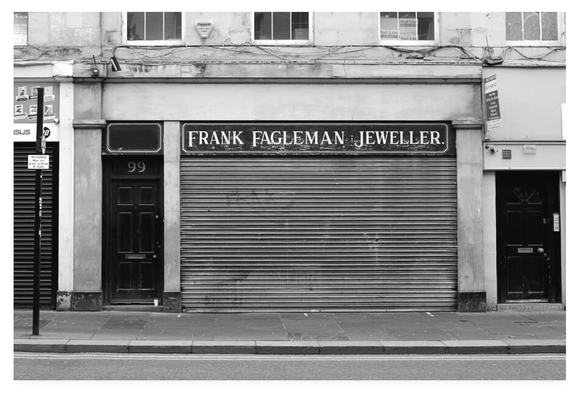 Black and white photograph of a closed jewellery shop with the metal shutter pulled down.