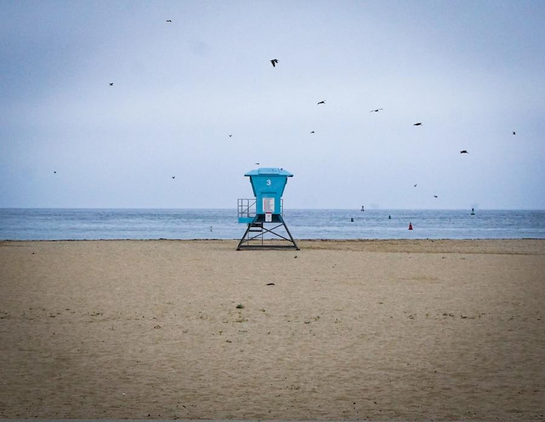 Long distance photo with a vignette effect of a lifeguard station on the beach overlooking the Pacific Ocean. Several seagull birds fly around and overhead the station. 

