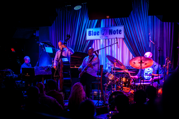 A jazz band performing on stage at Blue Note New York with an audience in the foreground.