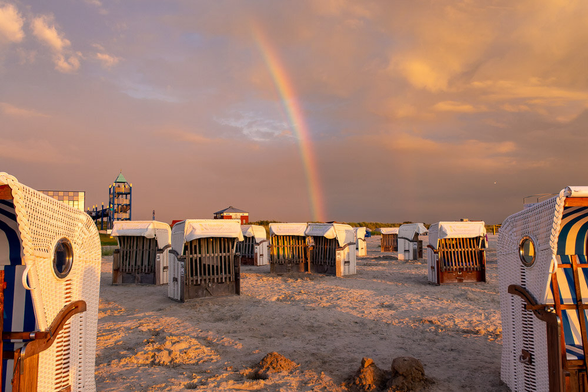 Strandkörbe an einem Strand, hinter einem Strandkorb endet ein Regenbogen.