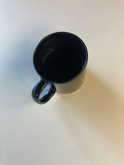Overhead view of a black coffee mug (with black coffee in it) sitting on a grey mat.