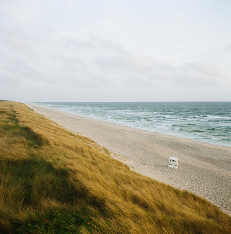 Square format photo of a beach with a single beach chair standing on it.