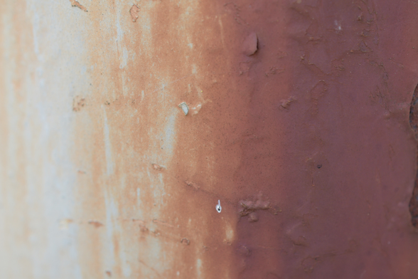 A closeup of a light pole showing a gradient from painted white to thoroughly rusted going from left to right.