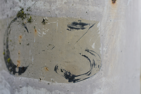 A close up of a light pole showing the remnants of a painted number 3 on a grey background.