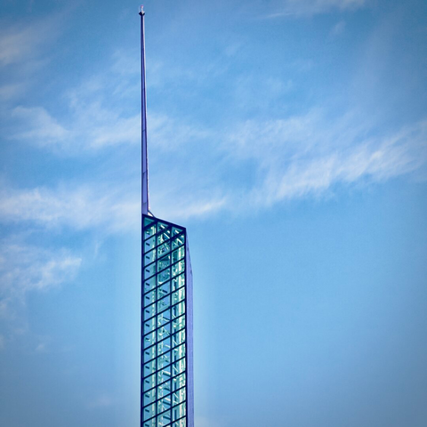 A three-sided glass tower shoots up into the partly cloudy blue sky, its antenna extending way past the top.