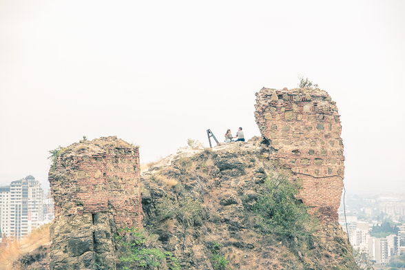 Eine alte Ruine hoch über der Stadt Tiflis, Georgien. Zwei Menschen sitzen dort, unterhalten sich und genießen den tollen Ausblick.