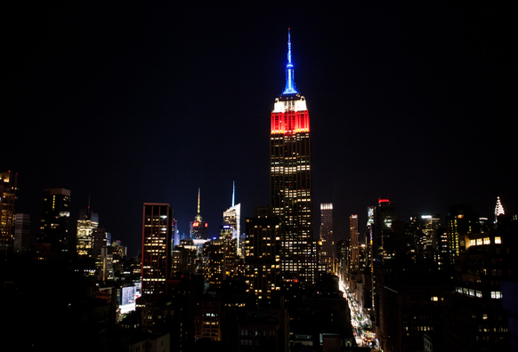 Nighttime cityscape with illuminated skyscrapers and a prominent building lit in red, white, and blue.