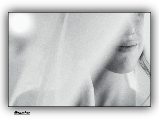 A black-and-white, blurred portrait of a young woman captured in an unconventional, fragmented composition. This time, only her lips, a part of her nose, and a loose strand of hair falling freely across her face are visible. A delicate, translucent curtain continues to obscure most of her features, evoking an atmosphere of intimacy and suggestion. The composition remains soft and subtle, with the blur and interplay of light and shadow enhancing the sense of ephemerality and poetic nuance.