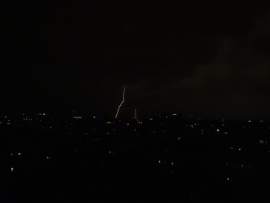 Photo prise la nuit. On y voit un éclair qui tombe derrière la Tour Eiffel.