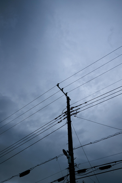 Silhouette of a utility pole with tangled power lines against a moody, cloudy blue sky.