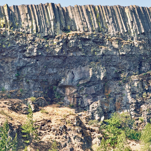 A large cliffside juts into the sky above, capped with many thin, vertical rock formations on a clear day.