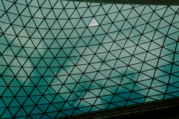 Vertical photo of the British Museum ceiling with one transparent triangle visible and clouds in the background.