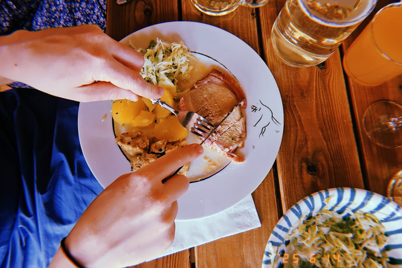 A person is cutting the braised pork on a white porcelain plate pictured from a birds eye view.