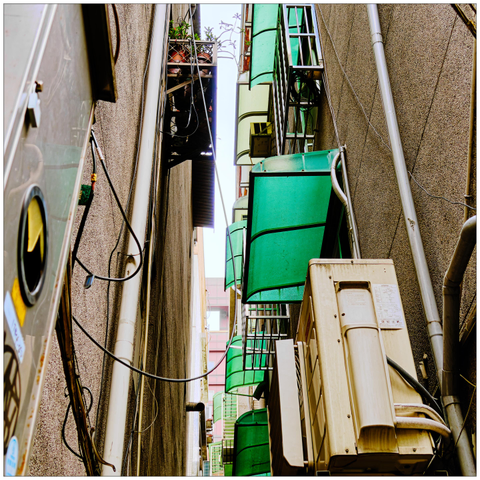 Looking up in a narrow alleyway full of pipes, AC units, plants, and rain covers.