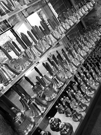 Photogtaphie en noir et blanc d'étagères pleines de cloches de tailles différentes, dans le magasin d'une fonderie.