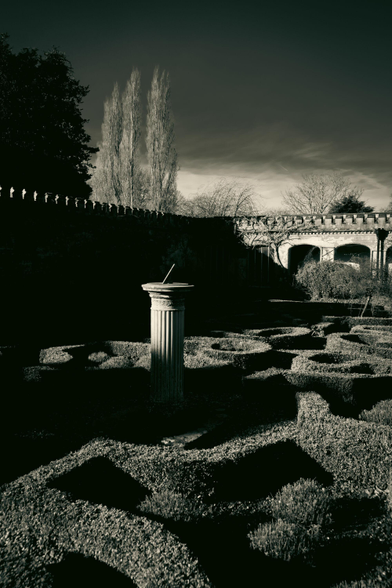 Walled garden at a stately manor; a sun dial in the centre of short, patterned hedges.