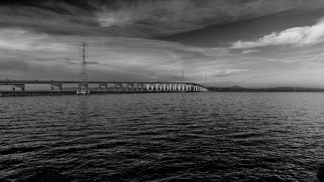 A very long but otherwise relatively unremarkable bridge crossing a large body of water. Power pylons run adjacent to the bridge.