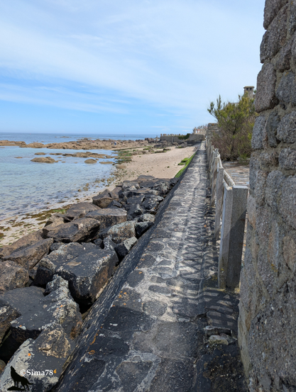 Allée étroite entre habitation à droite et mer sur la gauche.