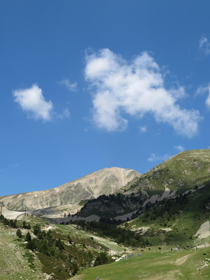 The image depicts a mountainous landscape under a clear blue sky with a few scattered white clouds. In the foreground, there is a grassy area with patches of green vegetation and a few small trees. The terrain is uneven, with rocky outcrops and a gentle slope leading up to the mountains. The mountains in the background are rugged, with exposed rock faces and some areas of sparse vegetation. A ski lift with cables and towers is visible on the left side of the image, suggesting the area is used for winter sports. The overall scene is serene and natural, with no visible human activity apart from the ski lift infrastructure.

Provided by @altbot, generated privately and locally using Ovis2-8B

🌱 Energy used: 0.175 Wh