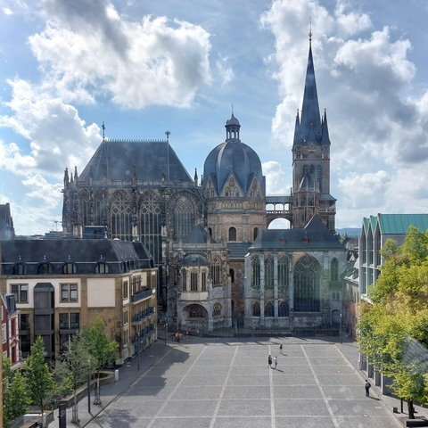 Der Dom zu Aachen, vom Rathaus aus gesehen. Die Sonne scheint, der Vorplatz ist fast menschenleer. Die komplexe bauliche Struktur der Kathedrale ist gut erkennbar.