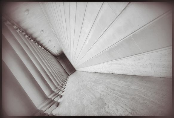 A tilted, monochrome picture of a long passageway outside the Legion of Honor in San Francisco. One side of the passage is lined with 18 unfluted doric columns... the other with smooth blocks of stone. At the far end, in the distance, a featureless wall of stone in shadow. 

This is all about receding lines and minimalism and an architect who said "I don't know what to do with this space and they wouldn't let me put a doorway at the end so let's just leave it blank and come back to it later."